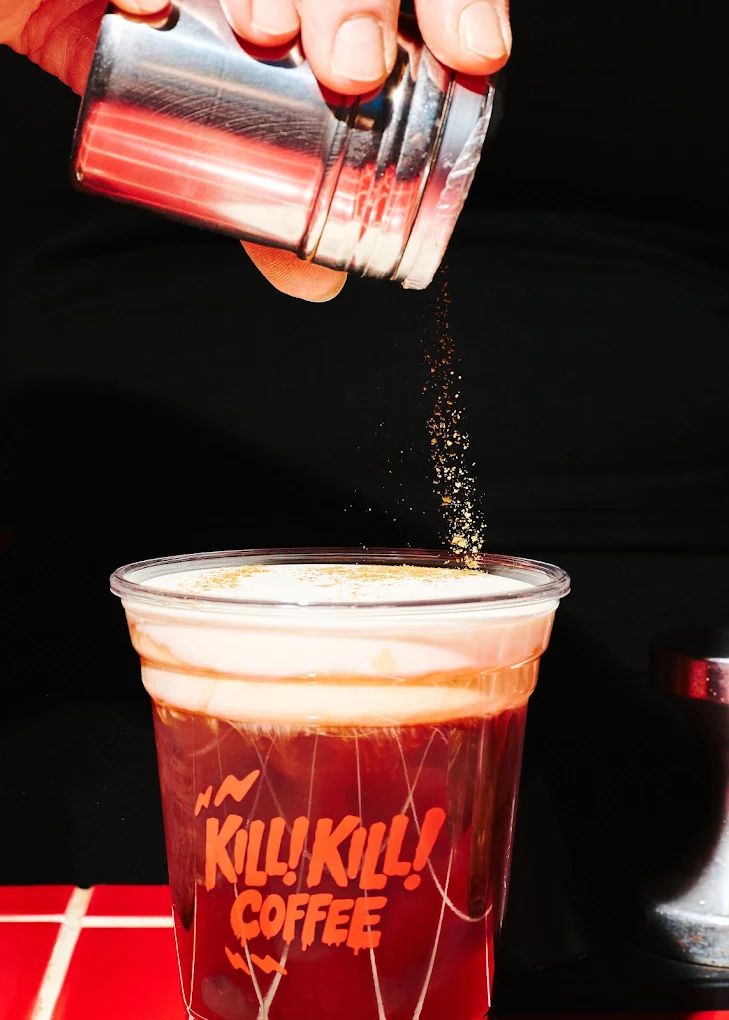 A finishing sprinkle over a cold foam coffee on the shop’s bright red counter