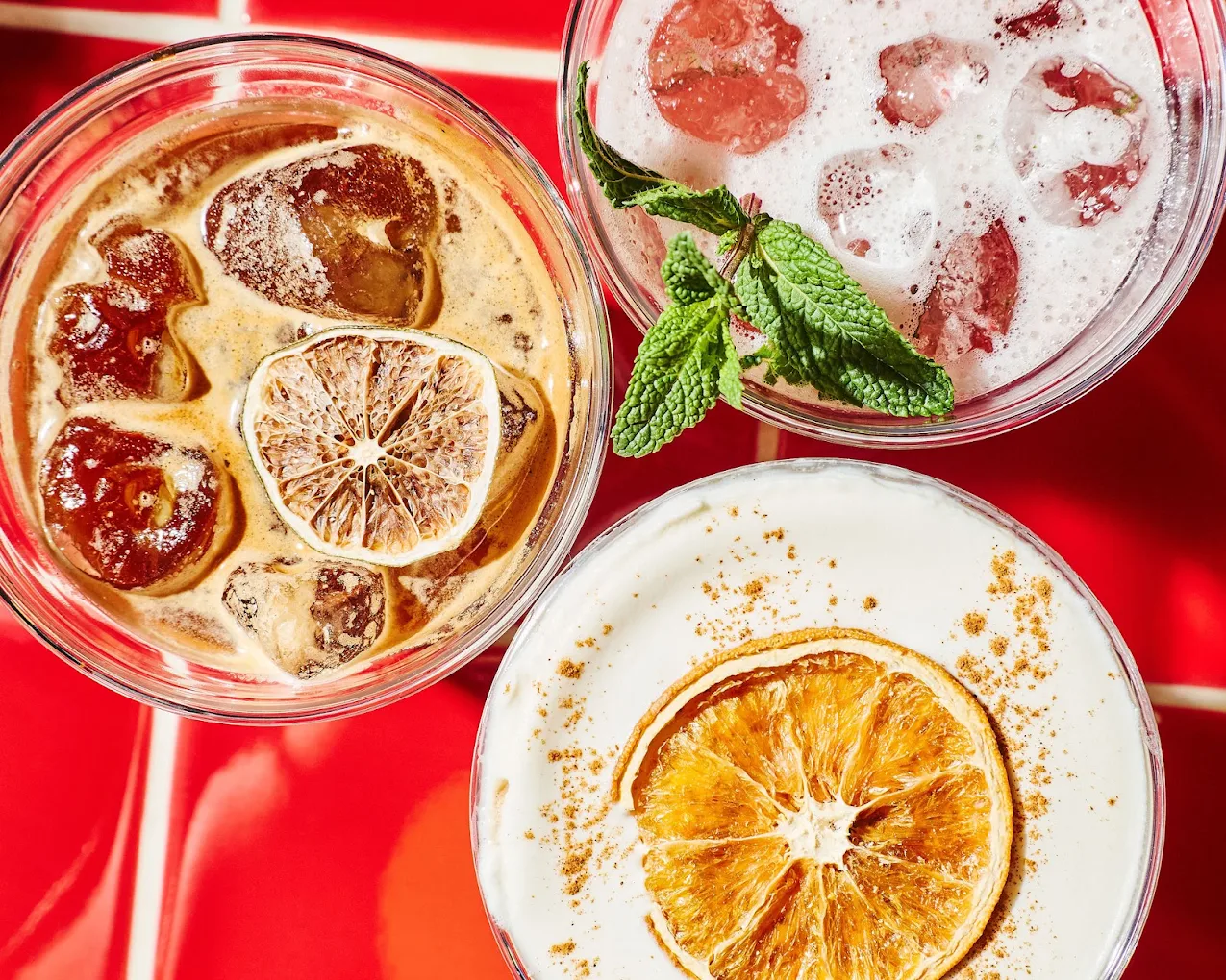 Three iced drinks with citrus and mint on the red tile counter