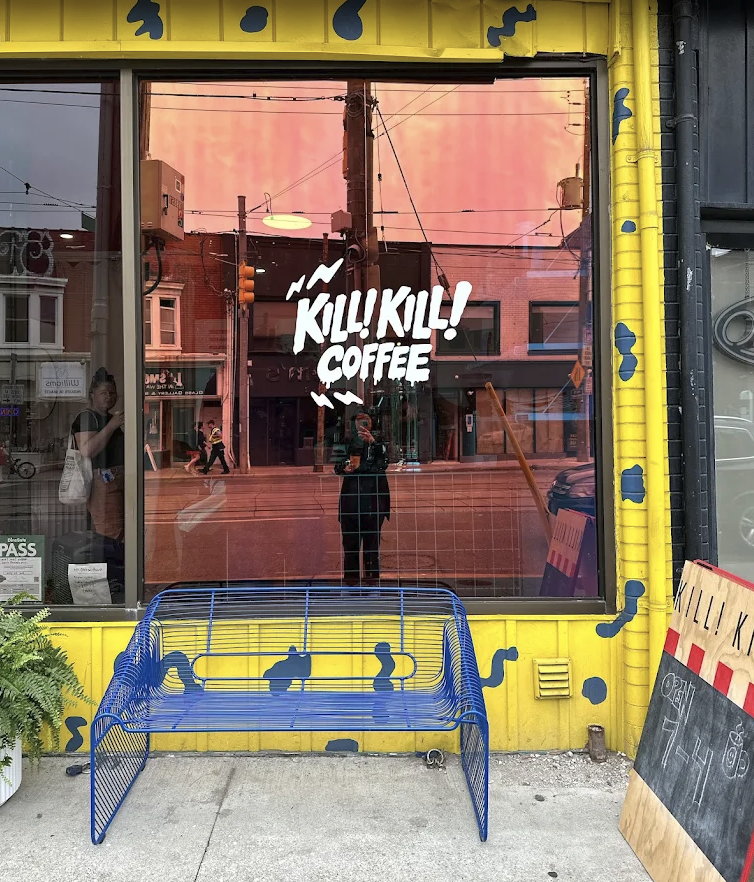 The yellow Kill! Kill! Coffee storefront with its blue bench on Dundas West